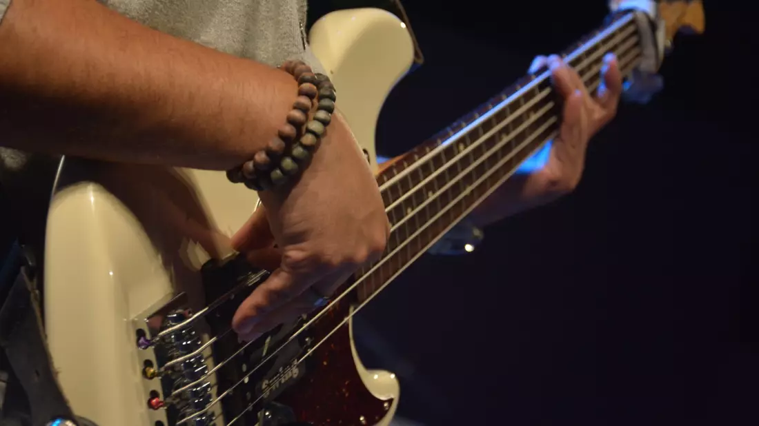 Bassist spielt weißen E-Bass, Hände an Saiten mit Armband in Nahaufnahme