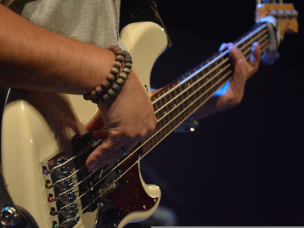 Groove in den Fingern: Mit Perlenarmband am Handgelenk zupft der Bassist die Saiten seines weißen E-Basses live auf der Bühne. - Foto: THN