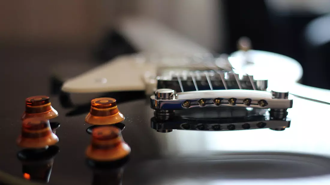 Detail einer schwarzen E-Gitarre mit Steg, Bernsteinreglern und Tonabnehmer