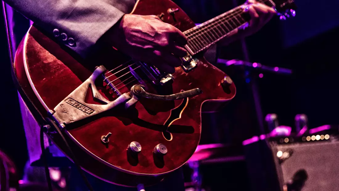 Musiker spielt rote Halbresonanz-E-Gitarre mit Vibratohebel im Bühnenlicht