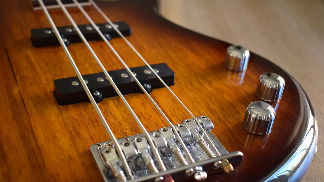 Detail eines fünfsaitigen E-Basses mit Tonabnehmern, Steg und Reglern in Sunburst