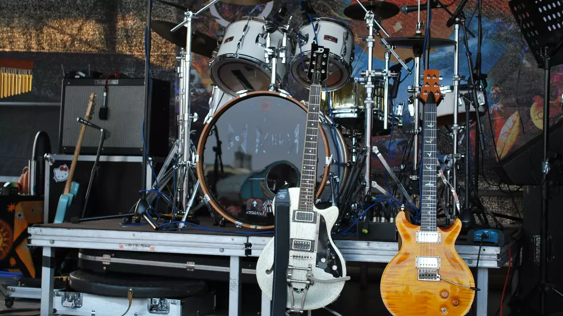 Bühne mit zwei E-Gitarren auf Ständern und Schlagzeug im Hintergrund bei Tag