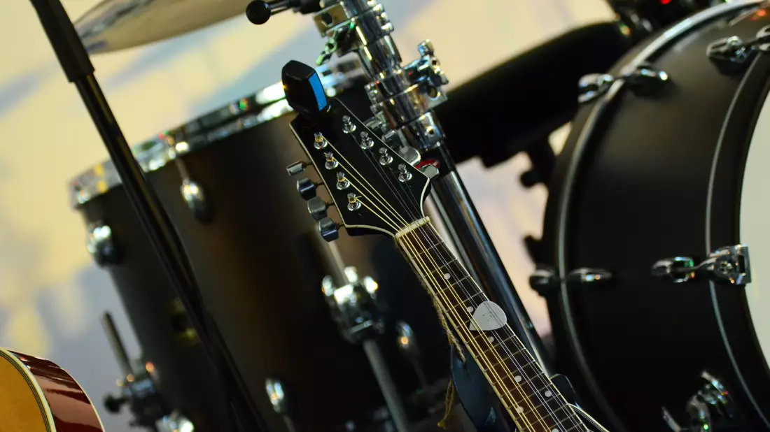 Kopfplatte einer zwölfsaitigen Gitarre vor unscharfem Schlagzeug im Hintergrund