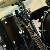 Stillleben aus Saiten und Fellen: Die Kopfplatte einer zwölfsaitigen Gitarre rückt vor dem verschwommenen Drumset in den Fokus. - Foto: THN
