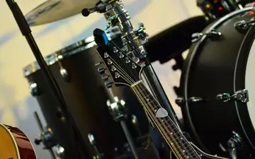 Stillleben aus Saiten und Fellen: Die Kopfplatte einer zwölfsaitigen Gitarre rückt vor dem verschwommenen Drumset in den Fokus. - Foto: THN