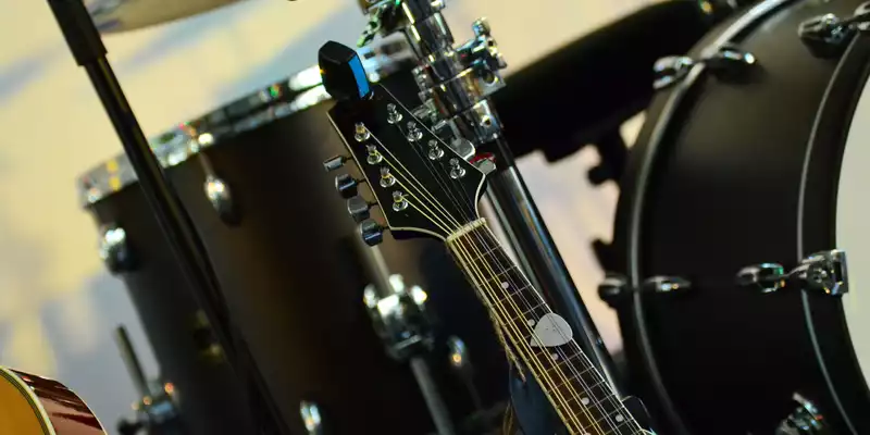 Stillleben aus Saiten und Fellen: Die Kopfplatte einer zwölfsaitigen Gitarre rückt vor dem verschwommenen Drumset in den Fokus. - Foto: THN