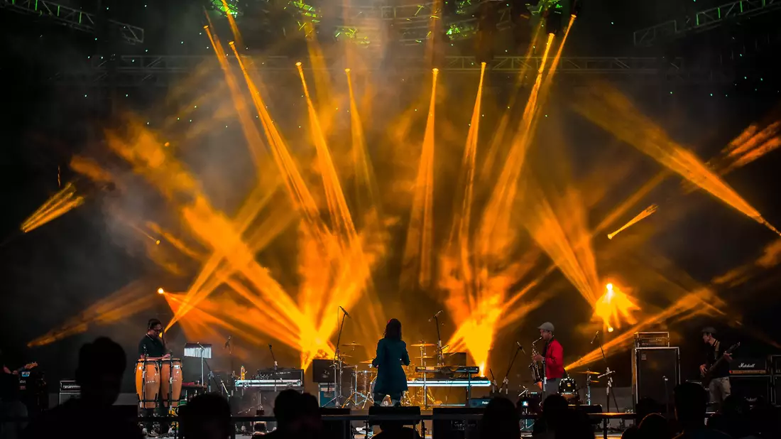 Band auf Bühne mit fächerförmigen orangen Lichtstrahlen und Nebel bei Konzert
