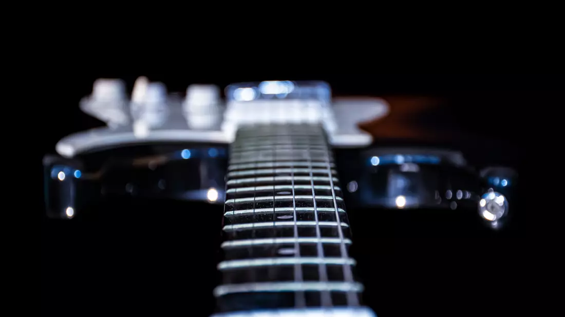 Blick entlang des Gitarrenhalses über Bünde und Saiten vor dunklem Hintergrund