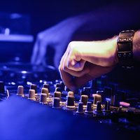 Feinabstimmung im Clublicht: Die Hände des DJs justieren die Regler des Mischpults, während Blau die Szene durchflutet. - Foto: THN
