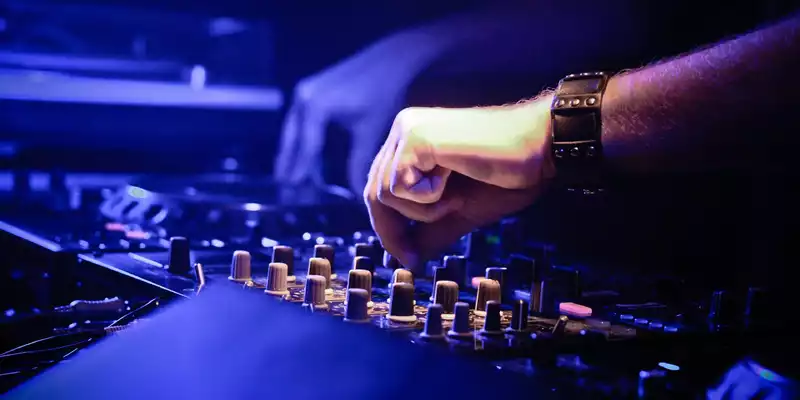 Feinabstimmung im Clublicht: Die Hände des DJs justieren die Regler des Mischpults, während Blau die Szene durchflutet. - Foto: THN