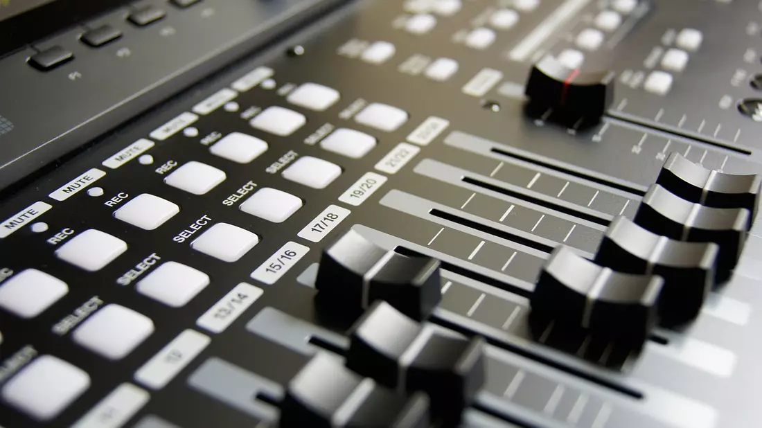 Nahaufnahme eines Mischpults mit Fadern, Tasten und Reglern im Tonstudio