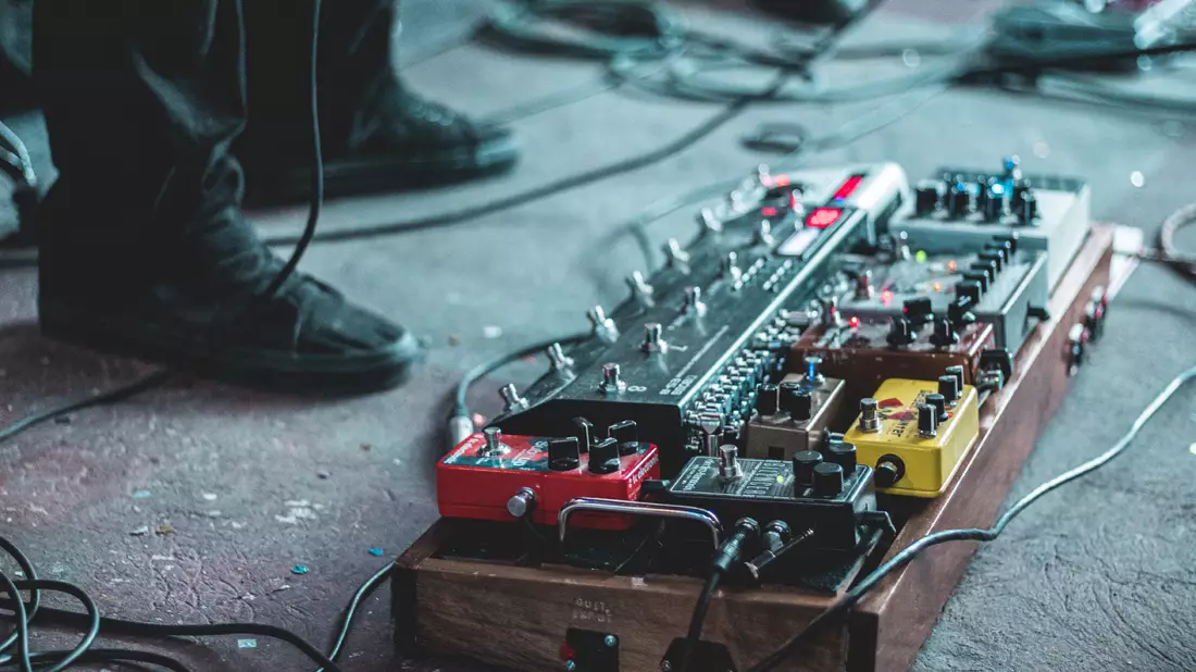Pedalboard mit mehreren bunten Effektpedalen und Kabeln am Bühnenboden