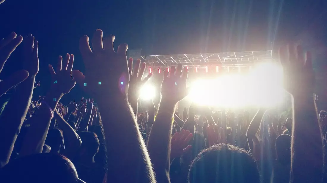 Erhobene Hände der Menge vor grell strahlenden Bühnenscheinwerfern bei Konzert