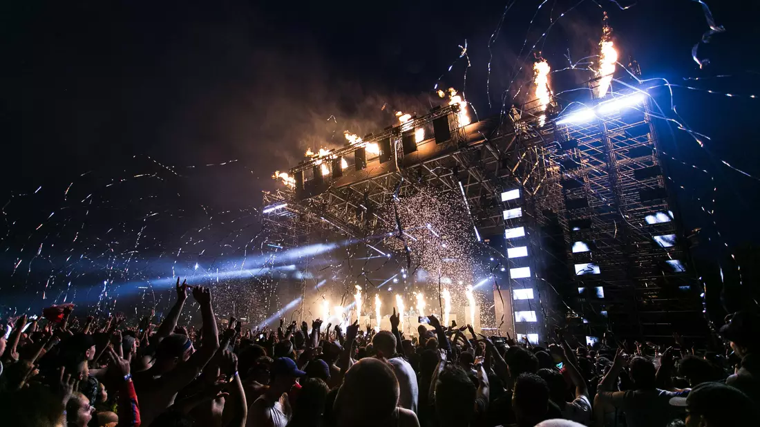 Festivalbühne bei Nacht mit Feuerfontänen, Konfetti und großer Menschenmenge