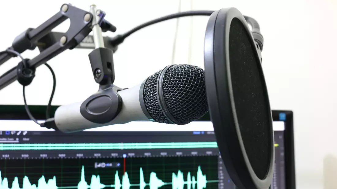 Studiomikrofon mit Popschutz an Mikrofonarm vor Bildschirm mit Audiowellenform