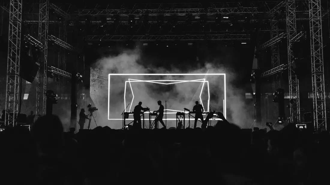 DJs als Silhouetten vor leuchtendem geometrischen Lichtrahmen in Schwarzweiß