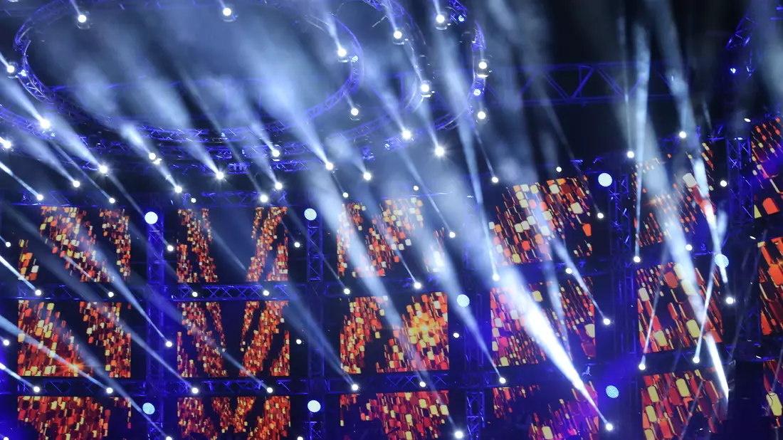 Bühne mit großer LED-Wand und vielen weiß-blauen Lichtstrahlen bei Konzert