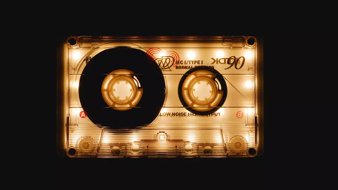 Goldglänzende durchscheinende Musikkassette vor schwarzem Hintergrund beleuchtet