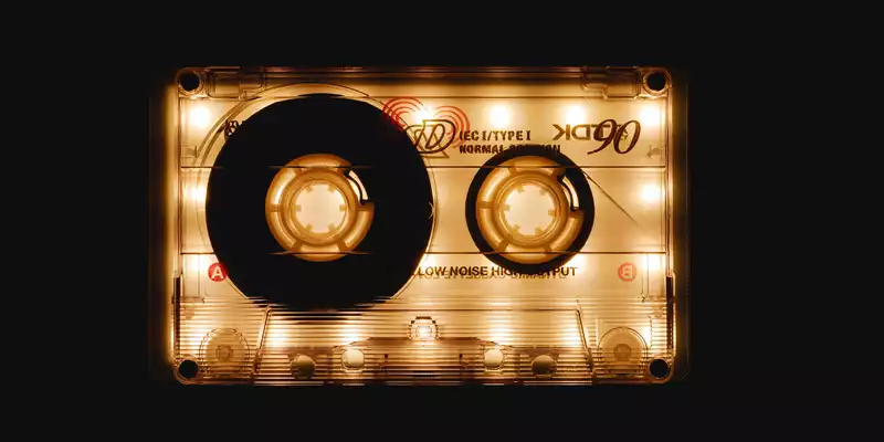 Retro-Charme im Glanz: Eine transparente Musikkassette leuchtet golden vor schwarzem Grund und beschwört die Achtziger herauf. - Foto: THN