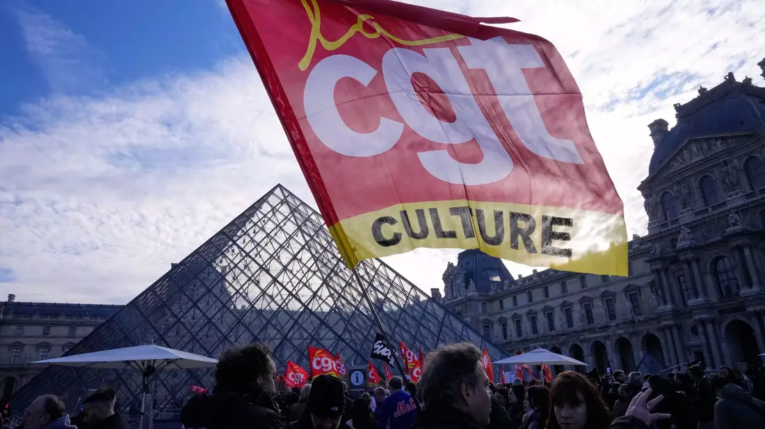 Angestellte zeigen Fahnen der Gewerkschaft CGT vor dem Louvre. - Bild: Michel Euler/AP/dpa