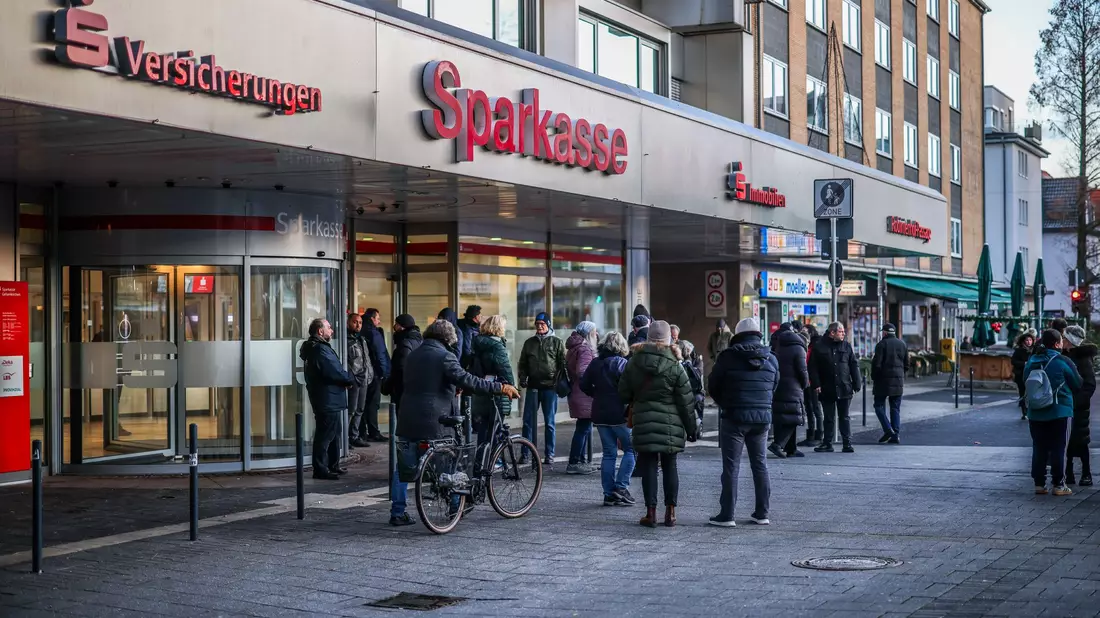 Polizisten sichern den Eingang der Sparkassenfiliale in Gelsenkirchen, vor der viele besorgte Kunde stehen und Informationen nach dem Einbruch in den Tresorraum verlangen. - Bild: Christoph Reichwein/dpa