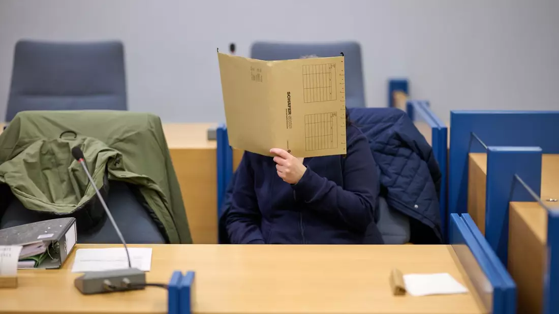 Die angeklagte Mutter verbirgt ihr Gesicht hinter einer Akte. Sie soll ihre kleine Tochter vom Kleinkindalter an versteckt und abgeschottet haben.  - Bild: Bernd Thissen/dpa