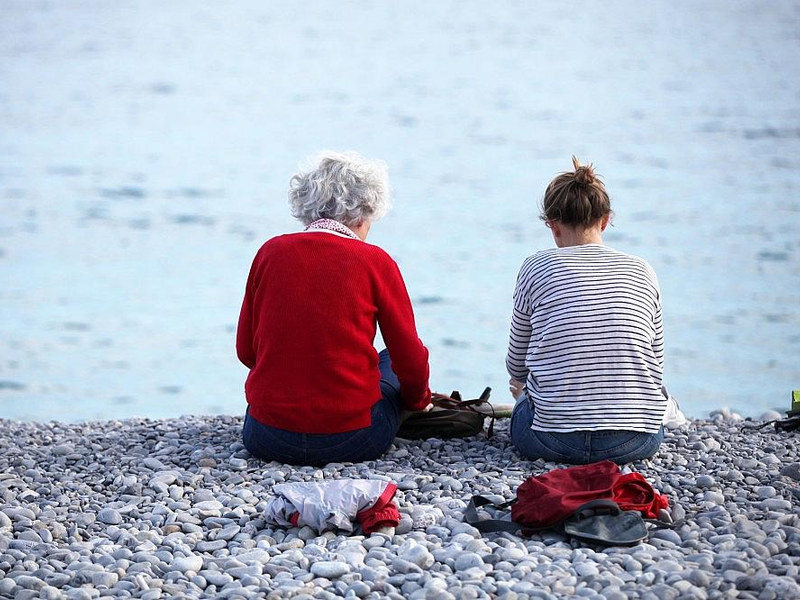 Alte und junge Frau sitzen am Strand - Foto: via dts Nachrichtenagentur
