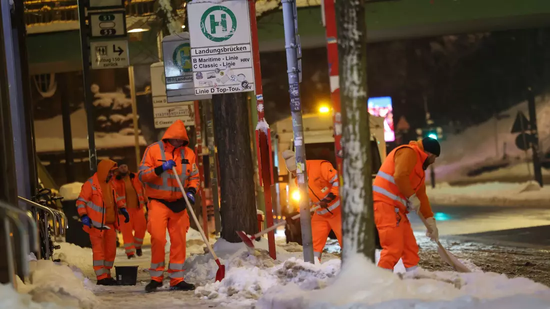 Mitarbeiter schieben Schnee von einem Bahnsteig am Hamburger Hauptbahnhof. - Bild: Christian Charisius/dpa