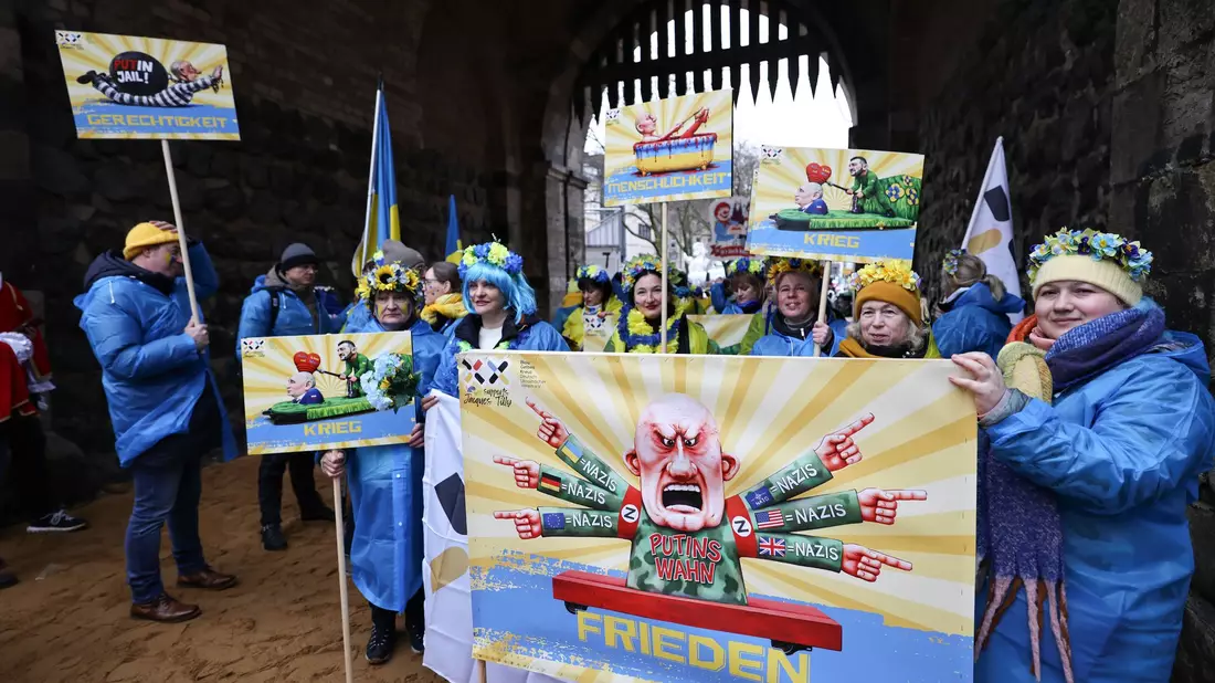 Der ukrainische Hilfsverein Blau-Gelbes-Kreuz hält Plakate mit Putin-Motiven hoch. Das ist als Zeichen der Solidarität mit Wagenbauer Jacques Tilly gemeint. Dieser wird in Russland strafrechtlich verfolgt.  - Bild: Oliver Berg/dpa