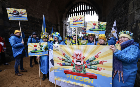 Der ukrainische Hilfsverein Blau-Gelbes-Kreuz hält Plakate mit Putin-Motiven hoch. Das ist als Zeichen der Solidarität mit Wagenbauer Jacques Tilly gemeint. Dieser wird in Russland strafrechtlich verfolgt.  - Foto: Oliver Berg/dpa