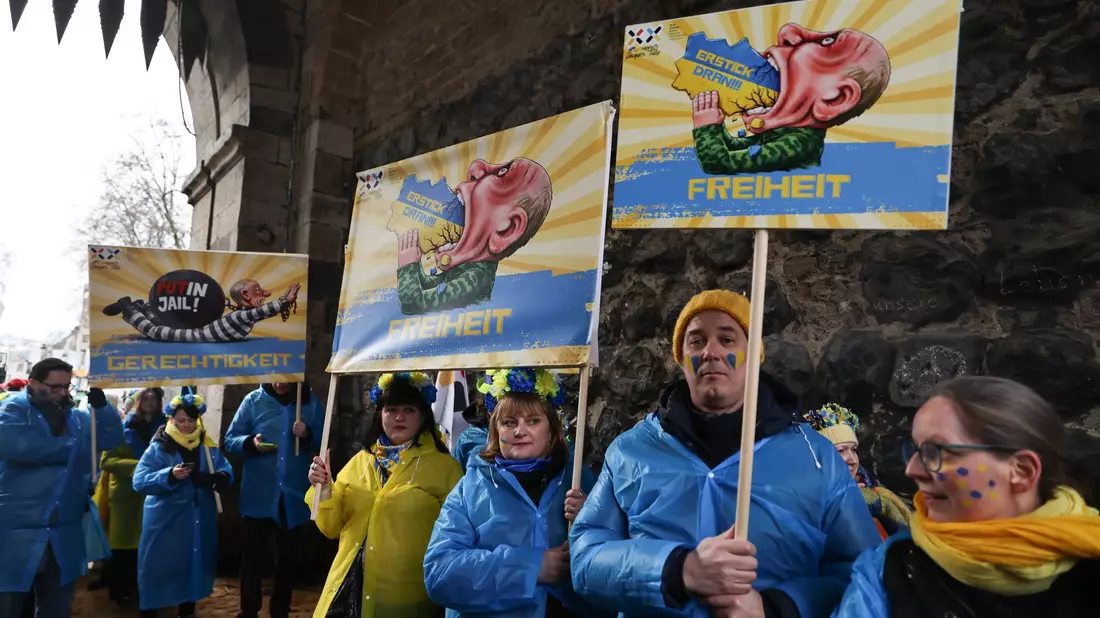 Mitglieder des ukrainischen Hilfsvereins Blau-Gelbes Kreuz halten im Kölner Rosenmontagszug Plakate mit früheren Putin-Darstellungen aus den Zügen in Köln und Düsseldorf hoch. - Bild: Oliver Berg/dpa