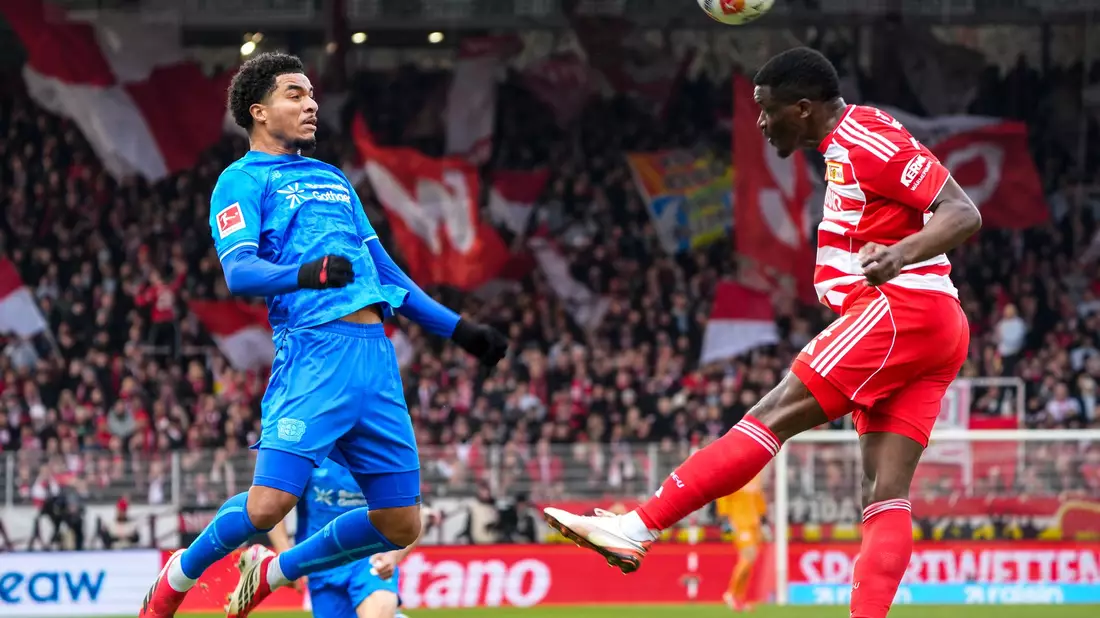 Union Berlins Nsoki (r.) setzt sich im Kopfballduell mit Leverkusens Tillmann (l.) durch.  - Bild: Soeren Stache/dpa