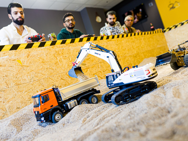 Gründer Siymo Othman (links) steuert mit Freunden kleine Bagger, Radlader und Lastwagen in seinem neu eröffneten Bagger-Café. Es soll das erste dieser Art in Deutschland sein. - Foto: Moritz Frankenberg/dpa