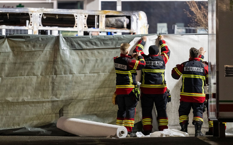 Feuerwehrleute verdecken den ausgebrannten Bus. - Foto: Alessandro Della Valle/KEYSTONE/dpa