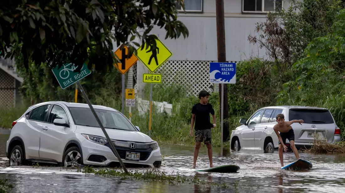 Zwei Jugendliche surfen in Waialua neben einem liegengebliebenen Fahrzeug im Hochwasser. - Bild: Stephen Lam/San Francisco Chronicle via AP/dpa