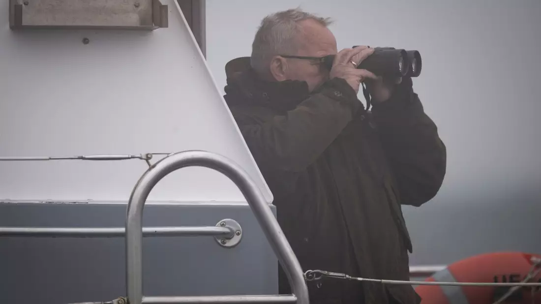 Mecklenburg-Vorpommerns Umweltminister Till Backhaus (SPD) steht mit einem Fernglas auf dem Polizeiboot «Uecker».  - Bild: Philip Dulian/dpa