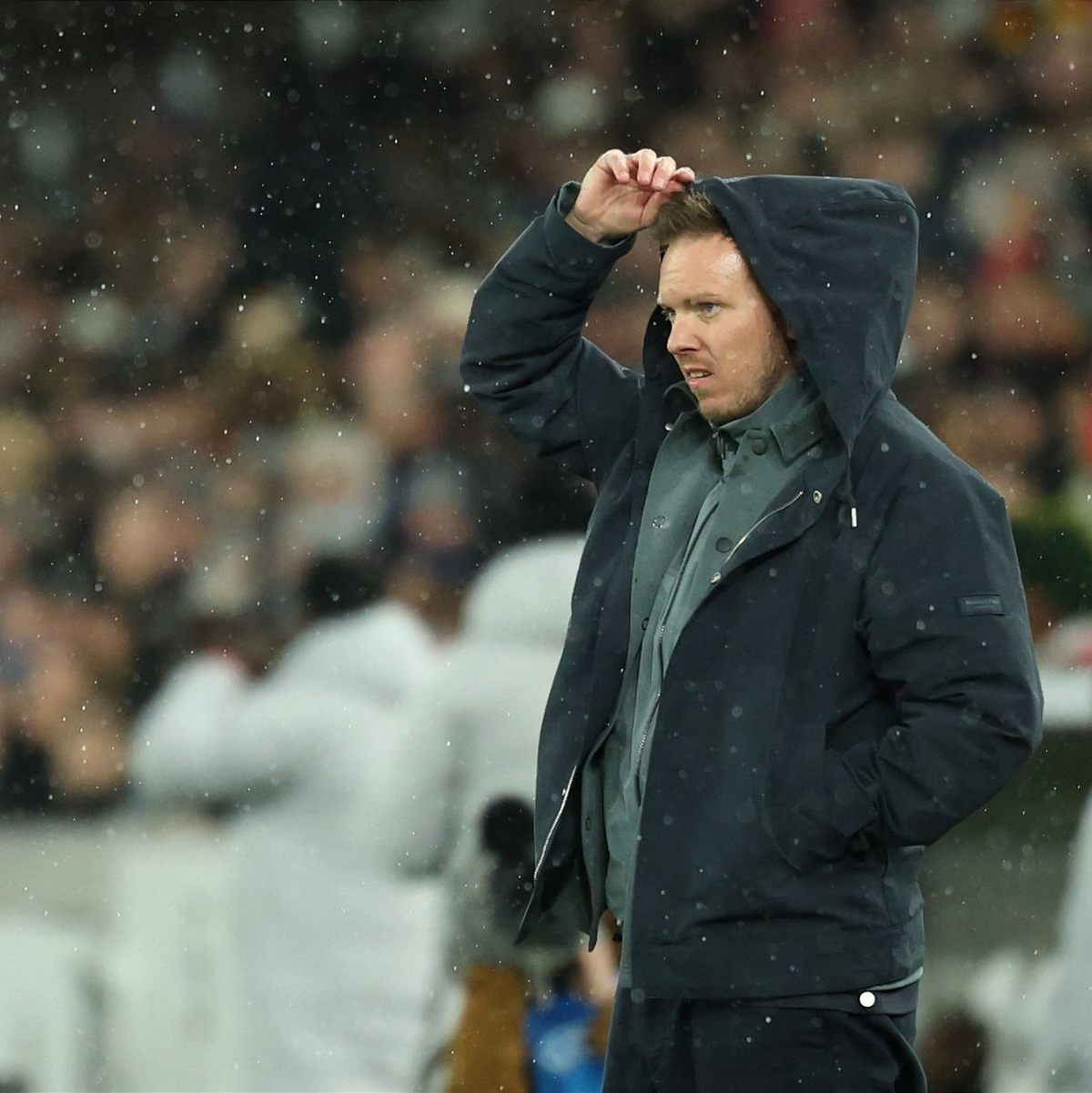 Julian Nagelsmann zieht sich im Regen eine Kapuze über den Kopf. - Foto: Christian Charisius/dpa