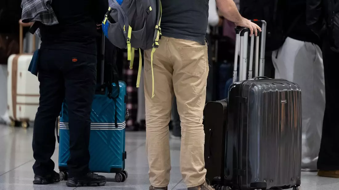 Passagiere stehen am Münchner Flughafen mit ihrem Gepäck an einem Check-in-Schalter. - Bild: Sven Hoppe/dpa