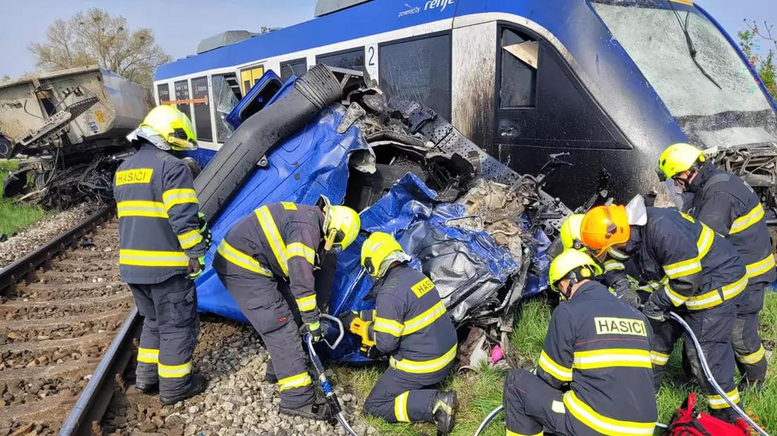 Feuerwehrleute arbeiten am Unglücksort, wo ein Personenzug und ein Lastwagen zusammengestoßen sind. Bei dem Unglück kam eine Person ums Leben, 21 Menschen wurden verletzt. - Bild: -/Feuerwehr- und Rettungsdienst Trnava/TASR/dpa