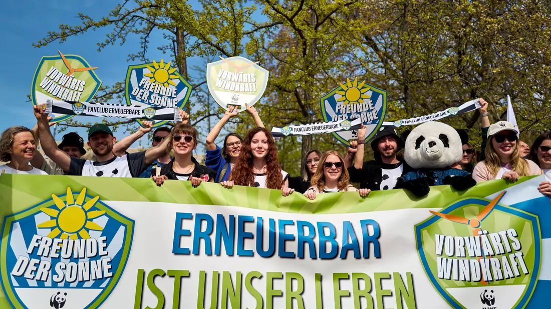 Demonstrierende halten ein Banner und Schilder in die Höhe, darunter eine Person im Pandakostüm. - Bild: Michael Ukas/dpa