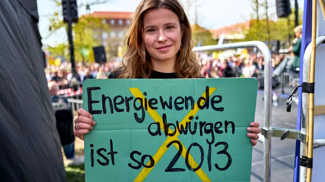 Luisa Neubauer hält ein Schild mit der Aufschrift «Energiewende abwürgen ist so 2013» in der Hand.  - Bild: Michael Ukas/dpa