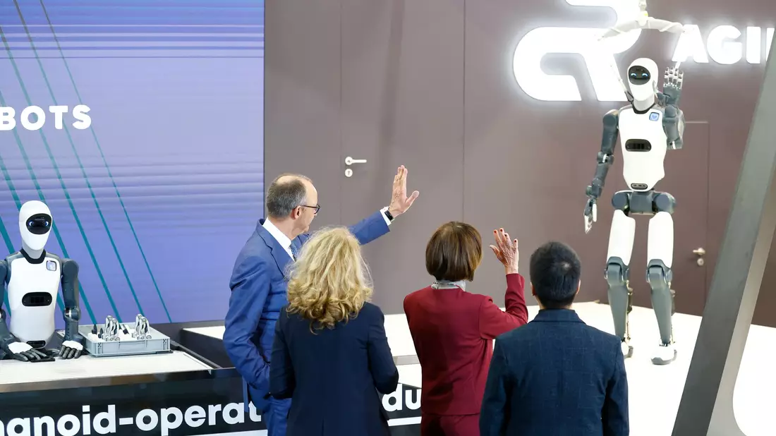 Bundeskanzler Friedrich Merz winkt einem Roboter zu – die Zukunft winkt zurück. - Bild: Michael Matthey/dpa