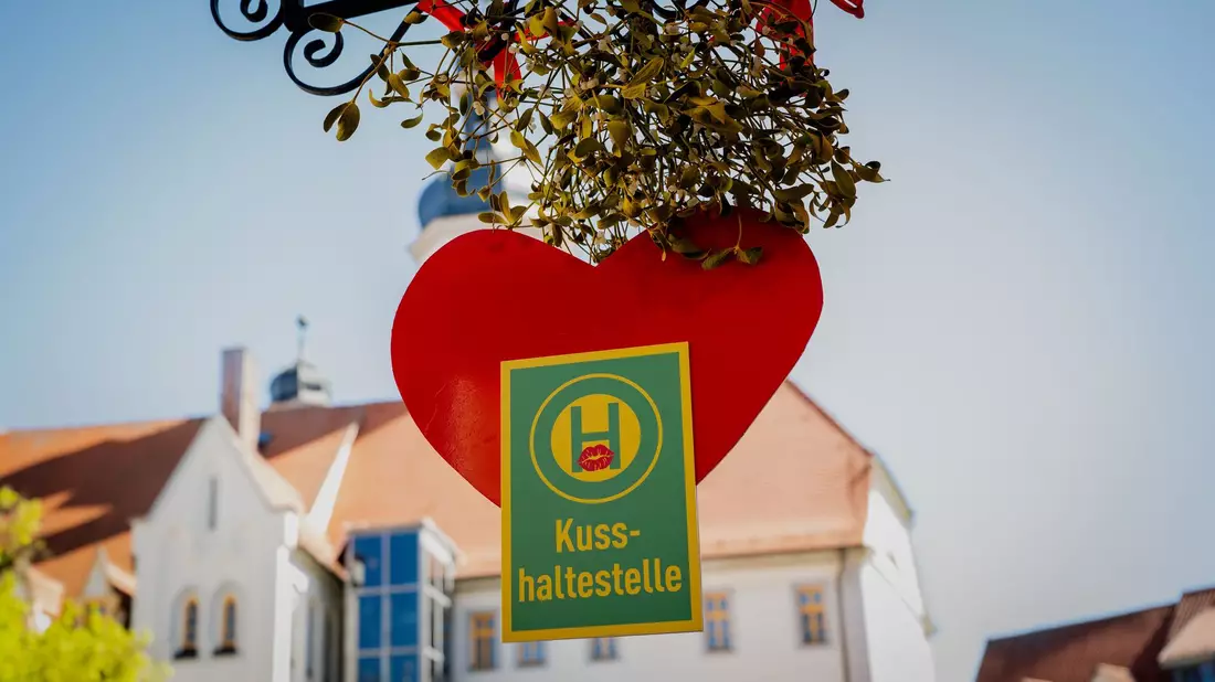 Rotes Herz und Mistelzweig: Auf dem Marktplatz in Eisenberg ist Küssen ausdrücklich erwünscht. - Bild: Jacob Schröter/dpa