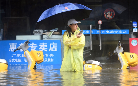Eine Frau steht in Qinzhou auf einer mit Wasser vollgelaufenen Straße. - Foto: Zhang Ailin/XinHua/dpa