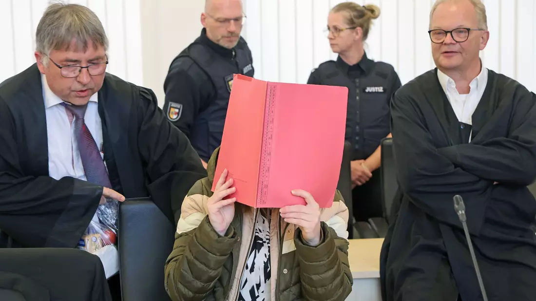Die Angeklagte sitzt mit Aktendeckel vor dem Gesicht zwischen ihren Verteidigern Andreas Ohm (l-r) und Thomas Löcker.  - Bild: Bernd Wüstneck/dpa