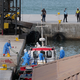 Gesundheitspersonal in Schutzkleidung evakuiert Patienten vom Kreuzfahrtschiff «Hondius» in einem Hafen.  - Foto: Misper Apawu/AP/dpa