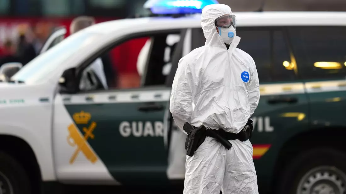 Die Sicherheitsvorkehrungen sind hoch: Ein Mitglied der Guardia Civil, das einen weißen Schutzanzug und Maske trägt, steht auf dem Hafengelände. - Bild: AP/dpa