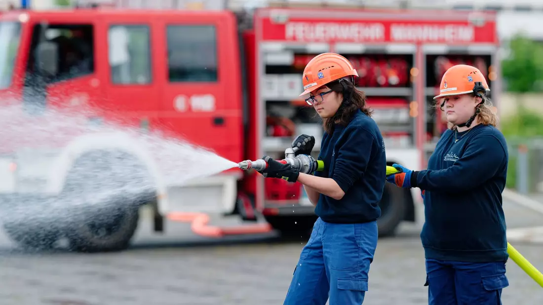 Ilias (links) und Annabella, Mitglieder der Jugendfeuerwehr in Mannheim, halten bei einer Übung einen Feuerwehrschlauch in den Händen. - Bild: Uwe Anspach/dpa