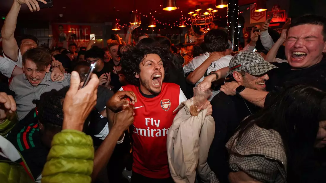 Arsenal-Anhänger feiern in einem Pub in der Nähe des Arsenal-Stadions, nachdem die Fußballmannschaft des FC Arsenal den Titel in der Premier League gewonnen hat. - Bild: Alberto Pezzali/AP/dpa