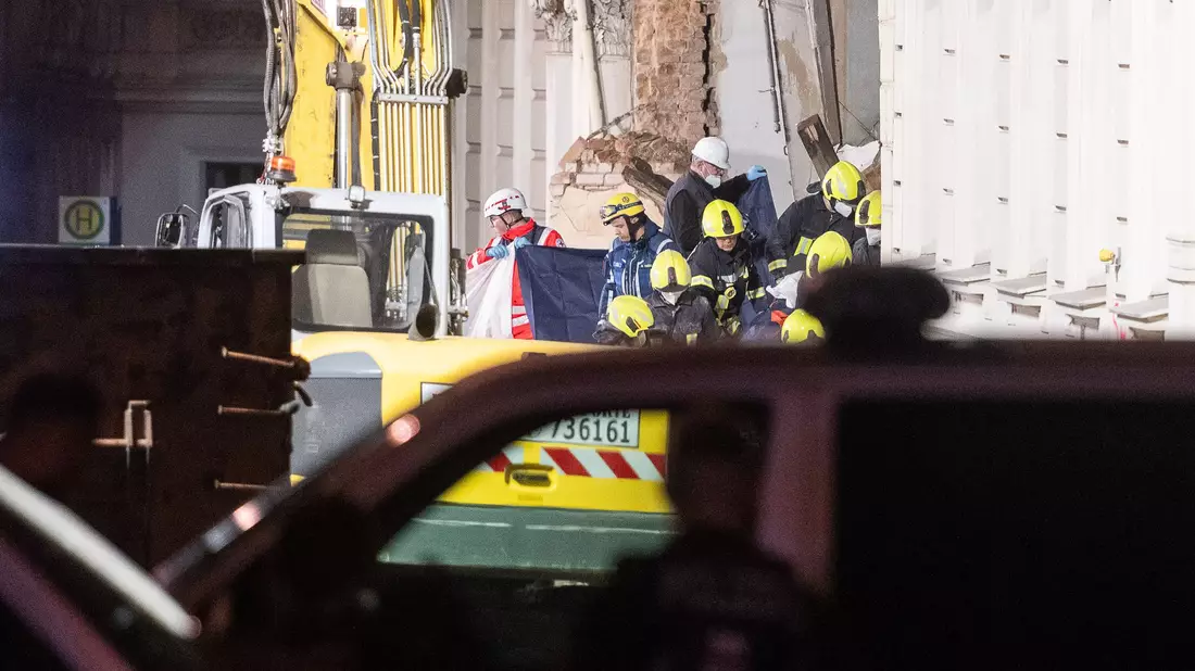 Einsatzkräfte der Feuerwehr trugen hinter Sichtschutz eine Leiche aus dem Trümmerfeld des eingestürzten Hauses. - Bild: Paul Glaser/dpa